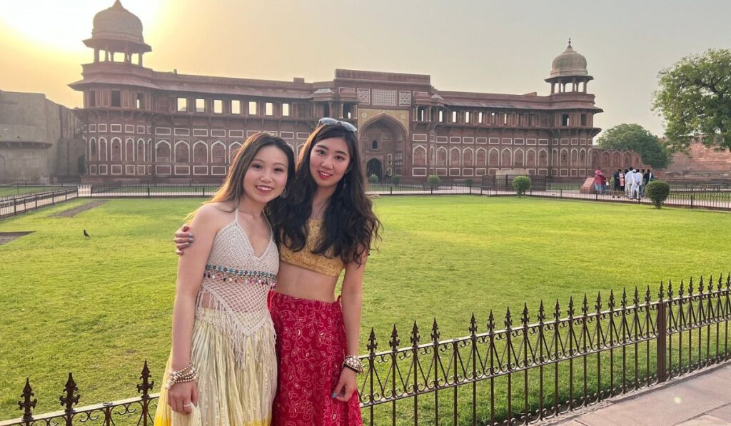 International tourists posing in front of the historic Red Fort in Delhi during a warm sunset, showcasing one of the city's most iconic landmarks.